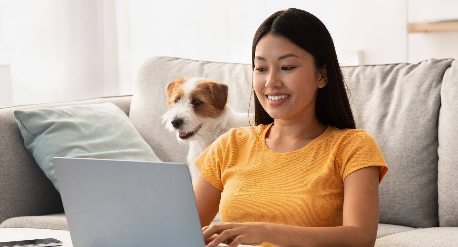 woman typing on laptop sitting with a jack russell terrier